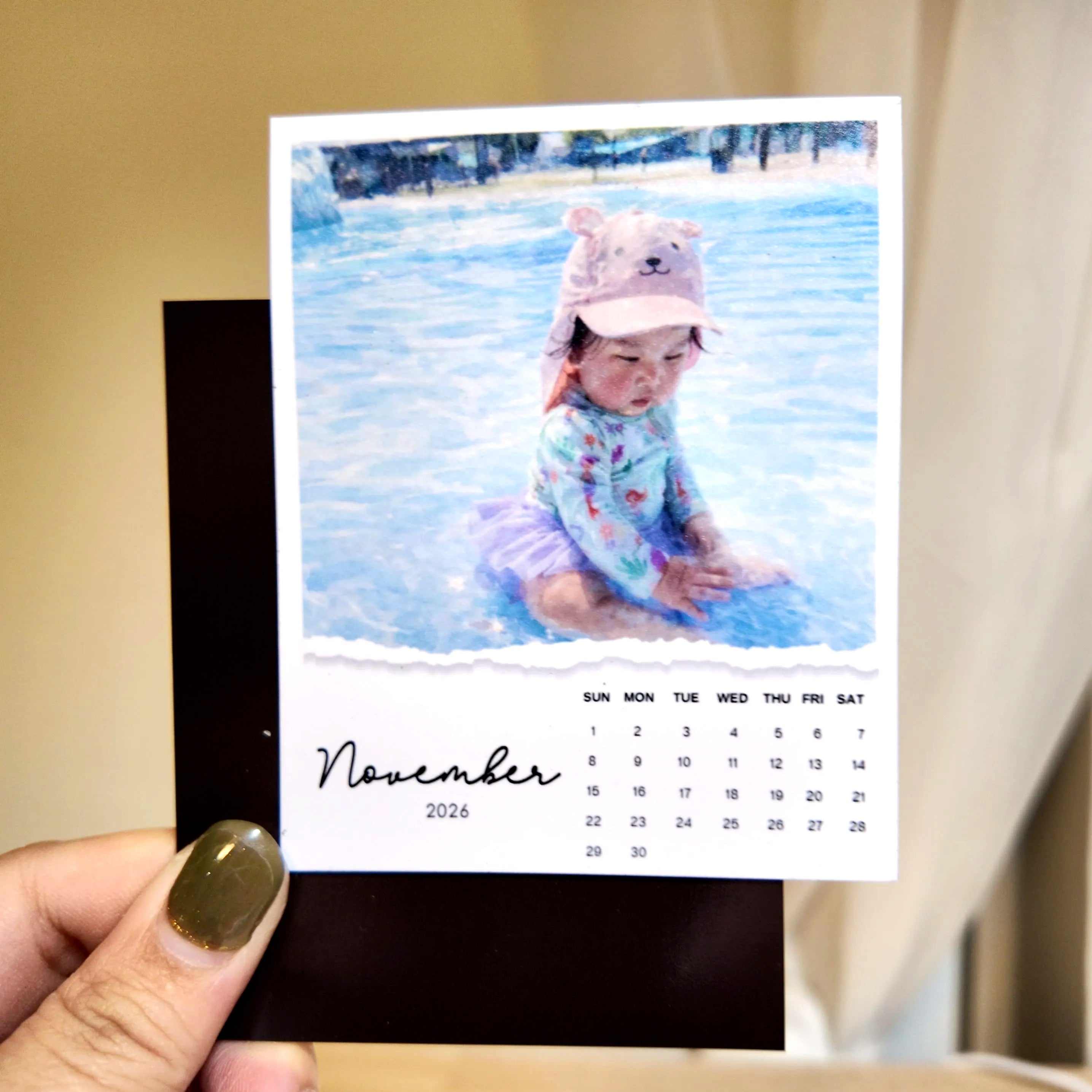 A hand holding a small calendar with a photo of a child sitting in a pool.
