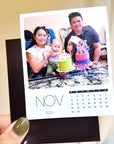A person holding a photo of a family celebrating a birthday, with two cakes and a baby present.