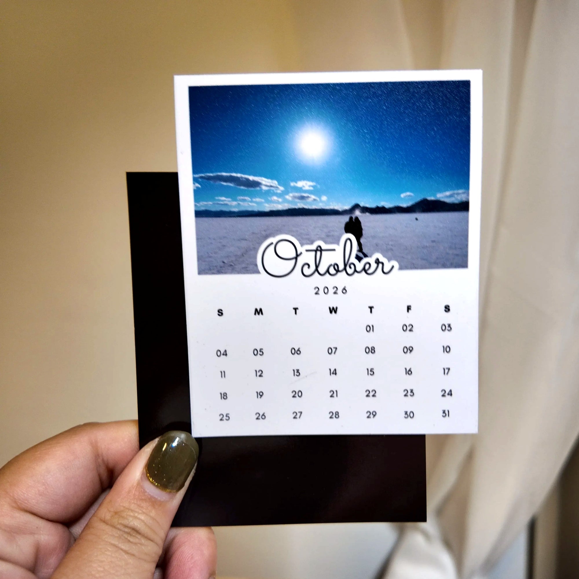 A person's hand holding a calendar for the month of October, with a scenic landscape visible in the background.