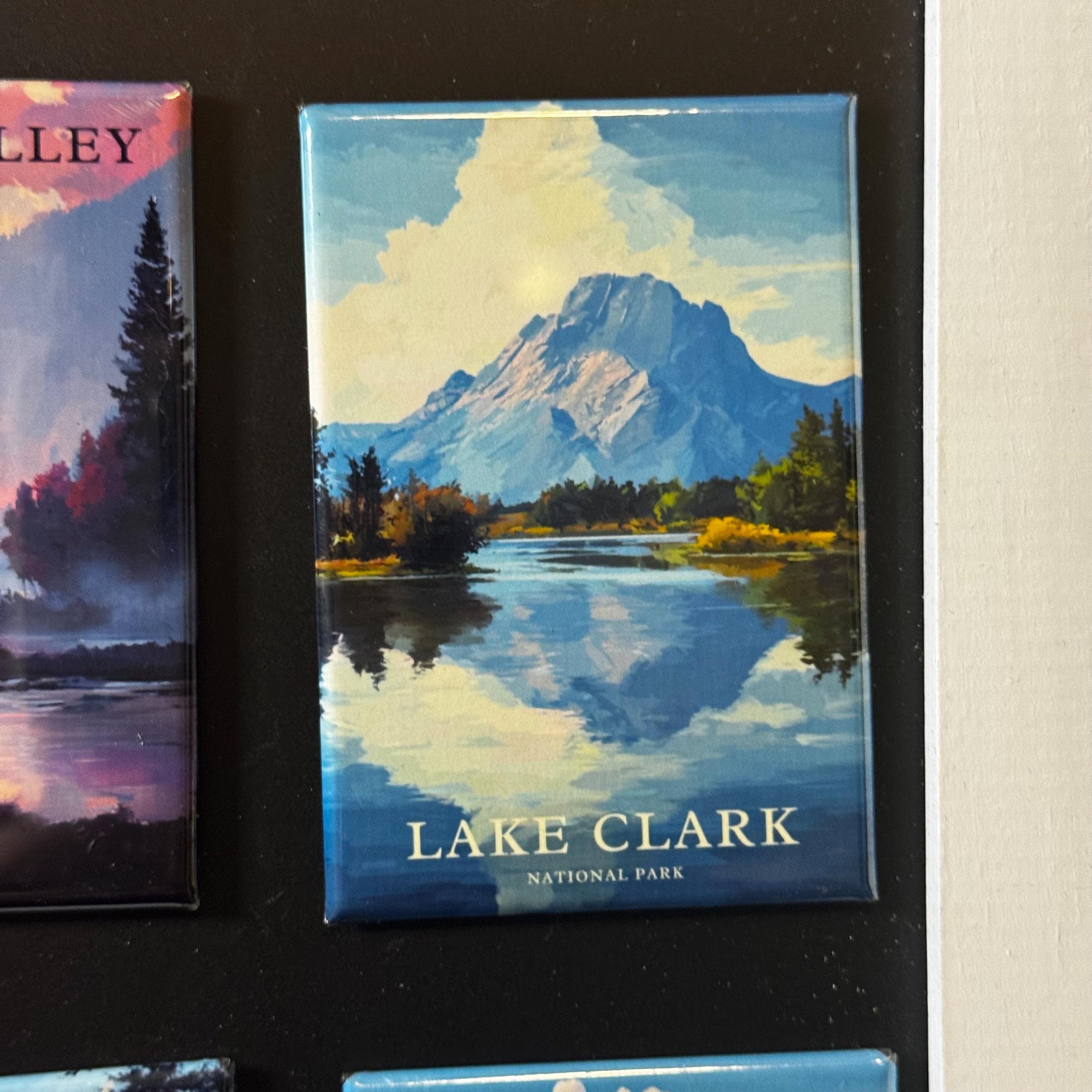 A magnet depicting Lake Clark National Park, with a mountain landscape and a lake in the foreground.